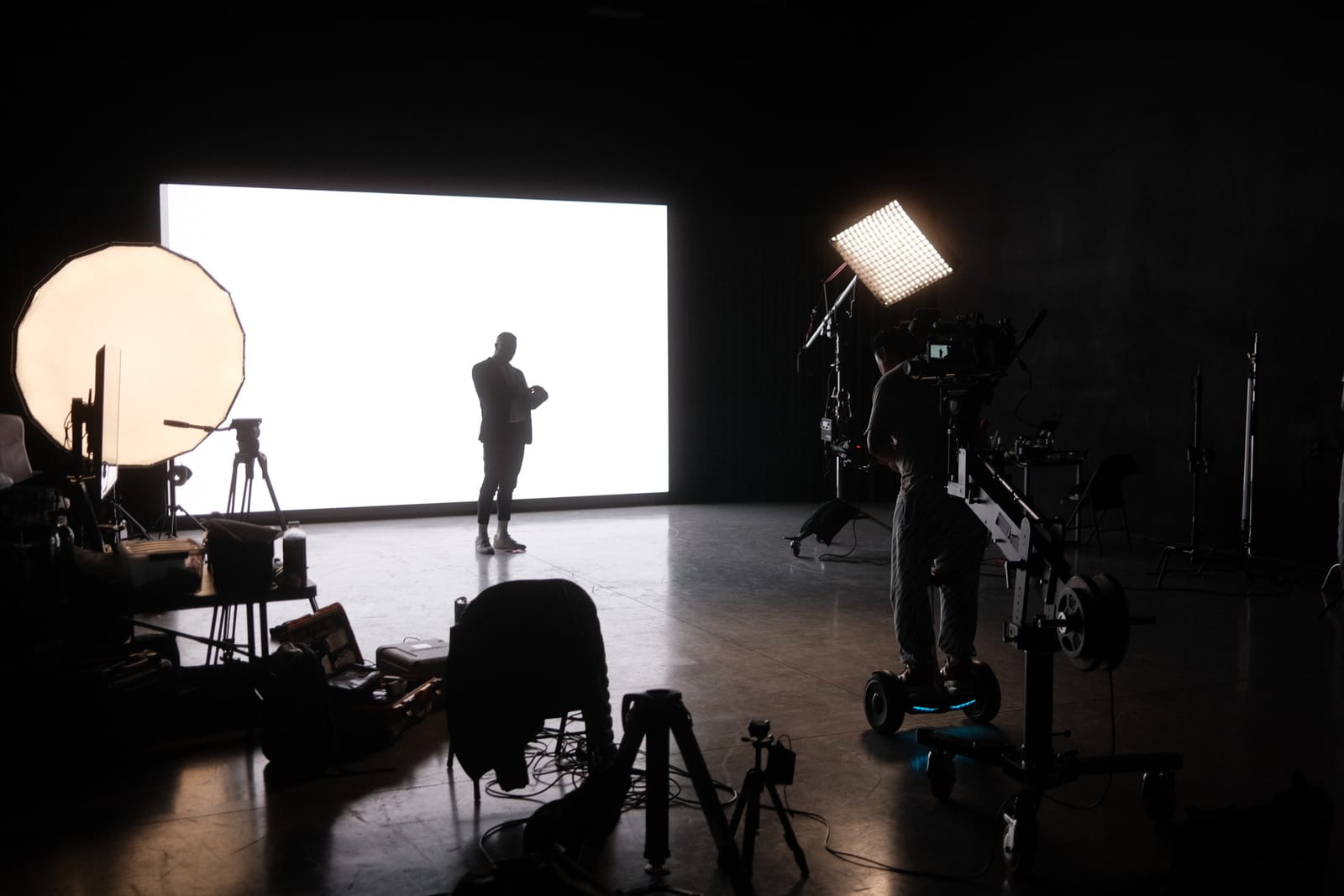 A camera operator on a dolly filming a suited subject against the lit LED wall