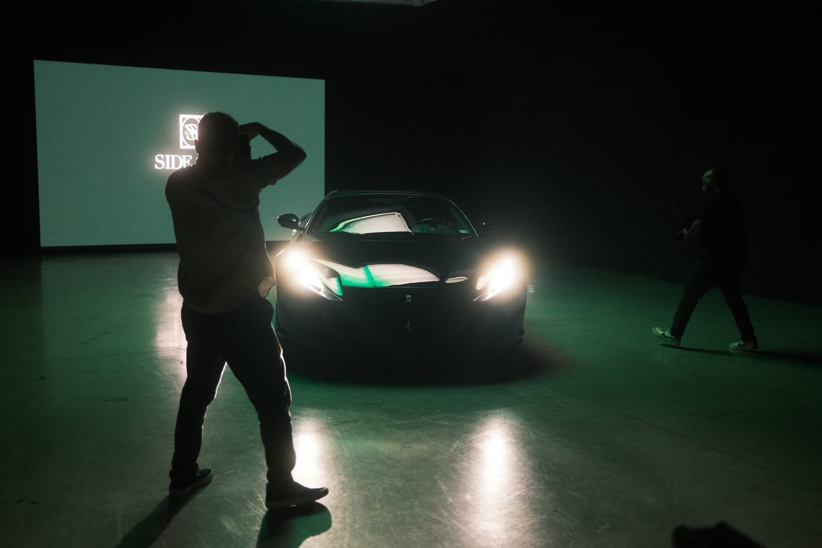 A crew filming a sports car on the studio floor with content playing on the LED wall behind it