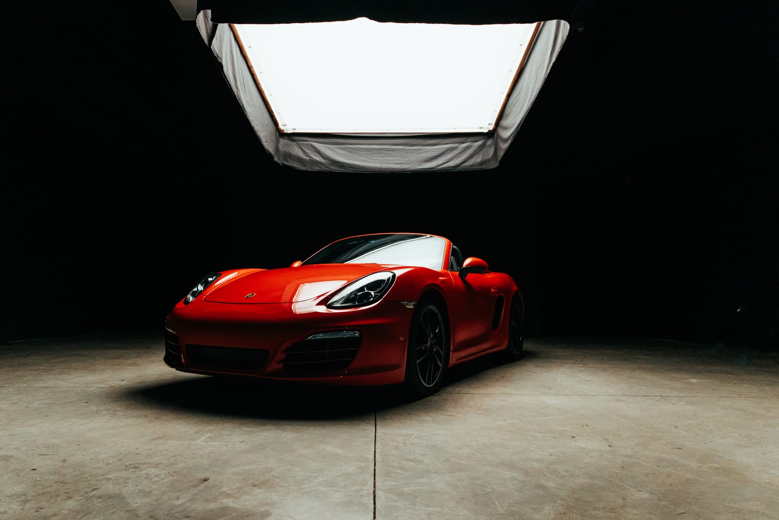 A red Porsche lit by a large overhead softbox on the studio floor